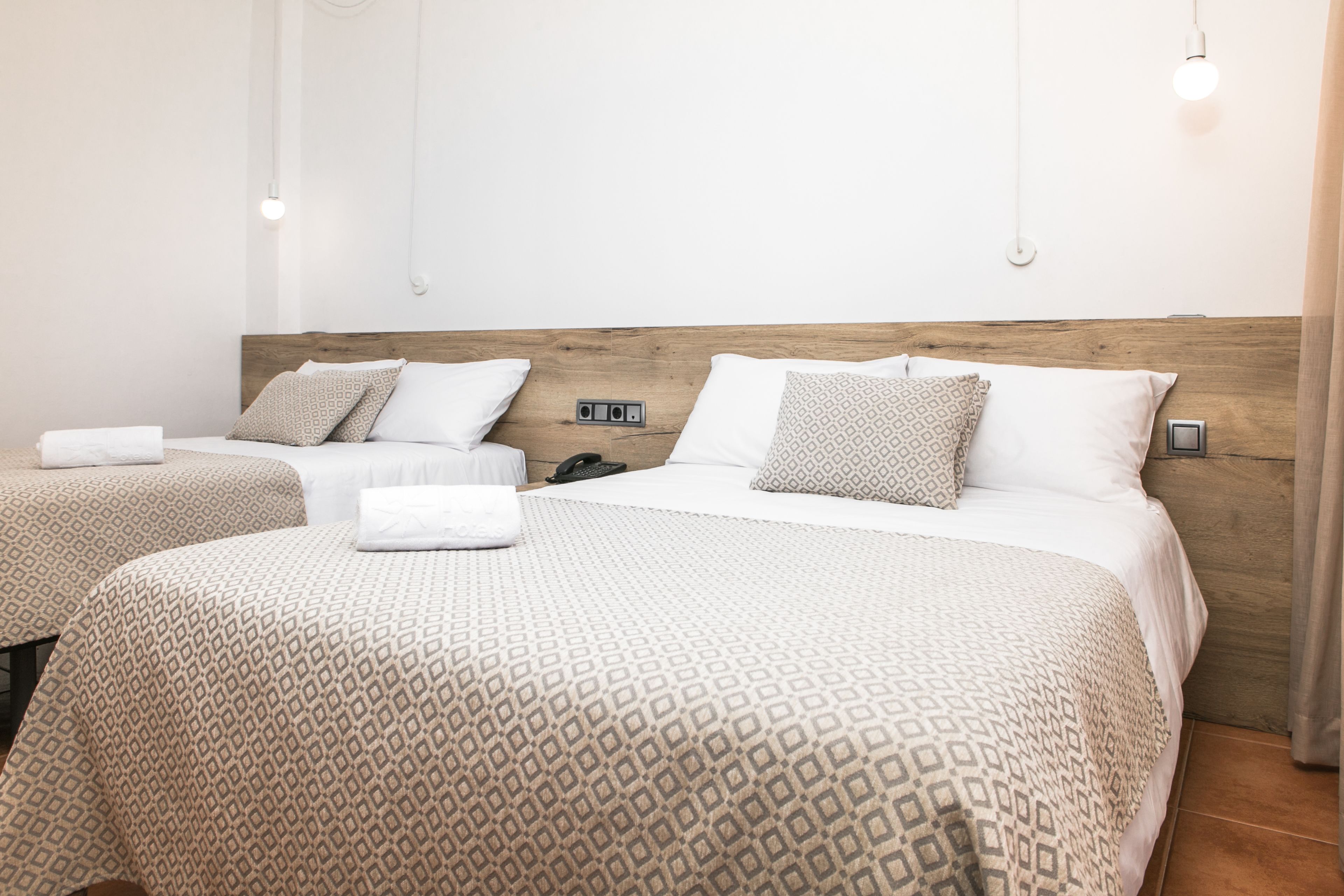 Camera d'albergo con due letti, ciascuno con copripiumini e cuscini decorati, una testiera in legno e un comodino con un telefono.