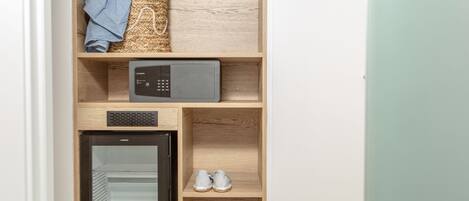 A compact kitchen with a microwave, a small refrigerator, and a shelf with shoes and a blue cloth.