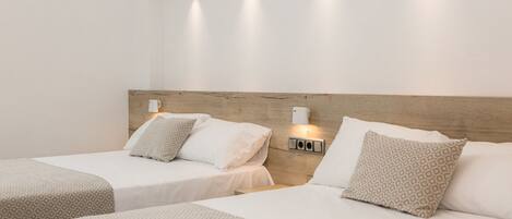 Habitación de hotel con dos camas, cada una con colcha y almohadas estampadas. Hay lámparas de pared sobre las camas.
