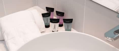 Un baño con un lavamanos blanco, una toalla blanca y tres tubos de productos para el cuidado de la piel.