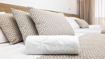 Una cama bien hecha con almohadillas estampadas y una toalla blanca enrollada con el nombre 'Hotels' bordado.