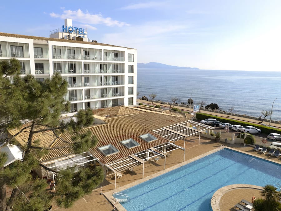 Un hotel con piscina, vistas al mar, y un edificio de varios pisos y balcones.