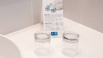 A bathroom with two empty glass containers on the sink and a sign about towel usage.