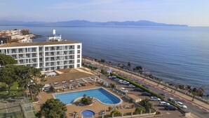 A hotel with a swimming pool, a view of the sea, and a parking area.