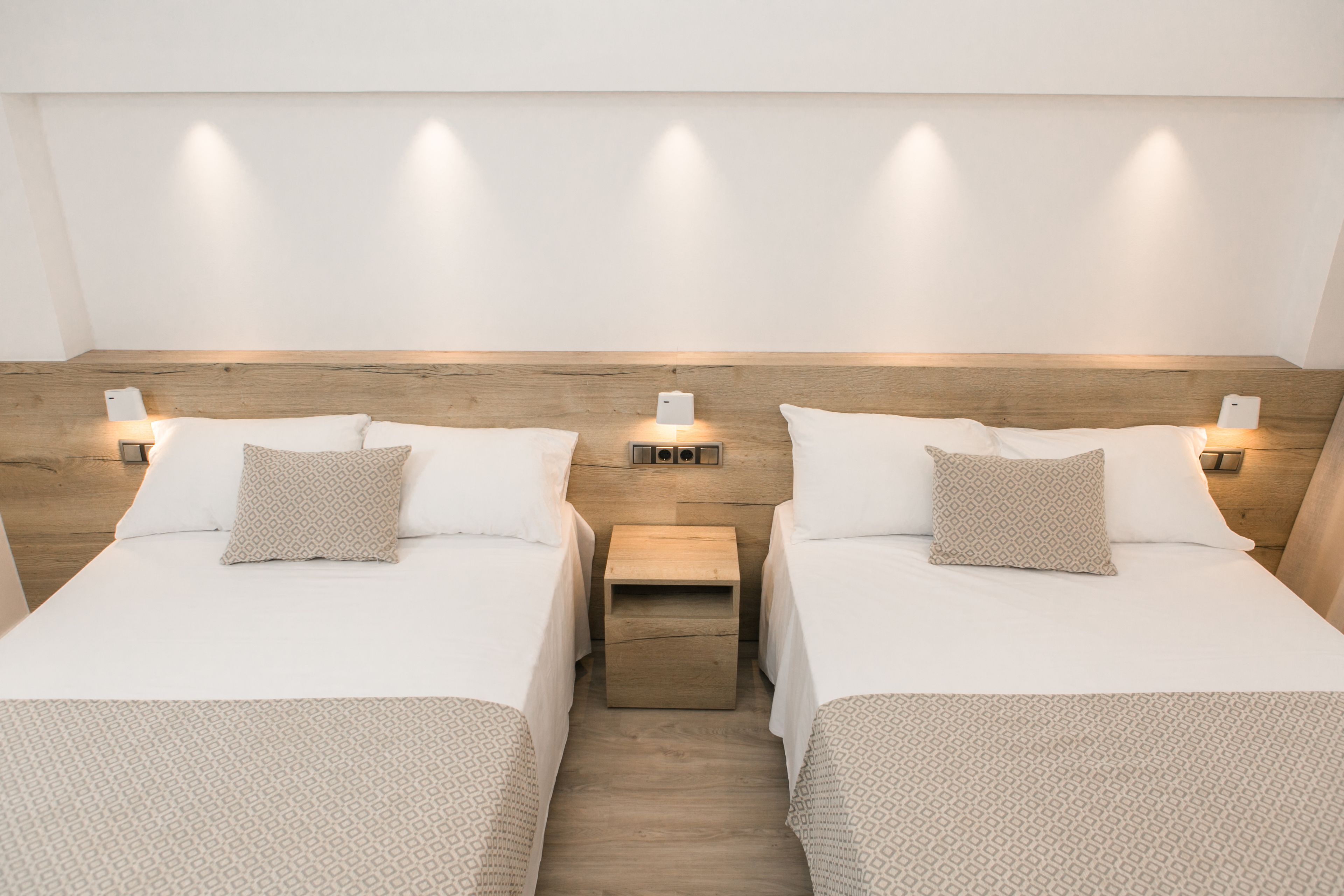 A hotel room with two beds, each with a wooden headboard, white bedding, and bedside lamps.