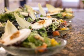A row of clear glass bowls filled with various salads, arranged on a granite countertop.