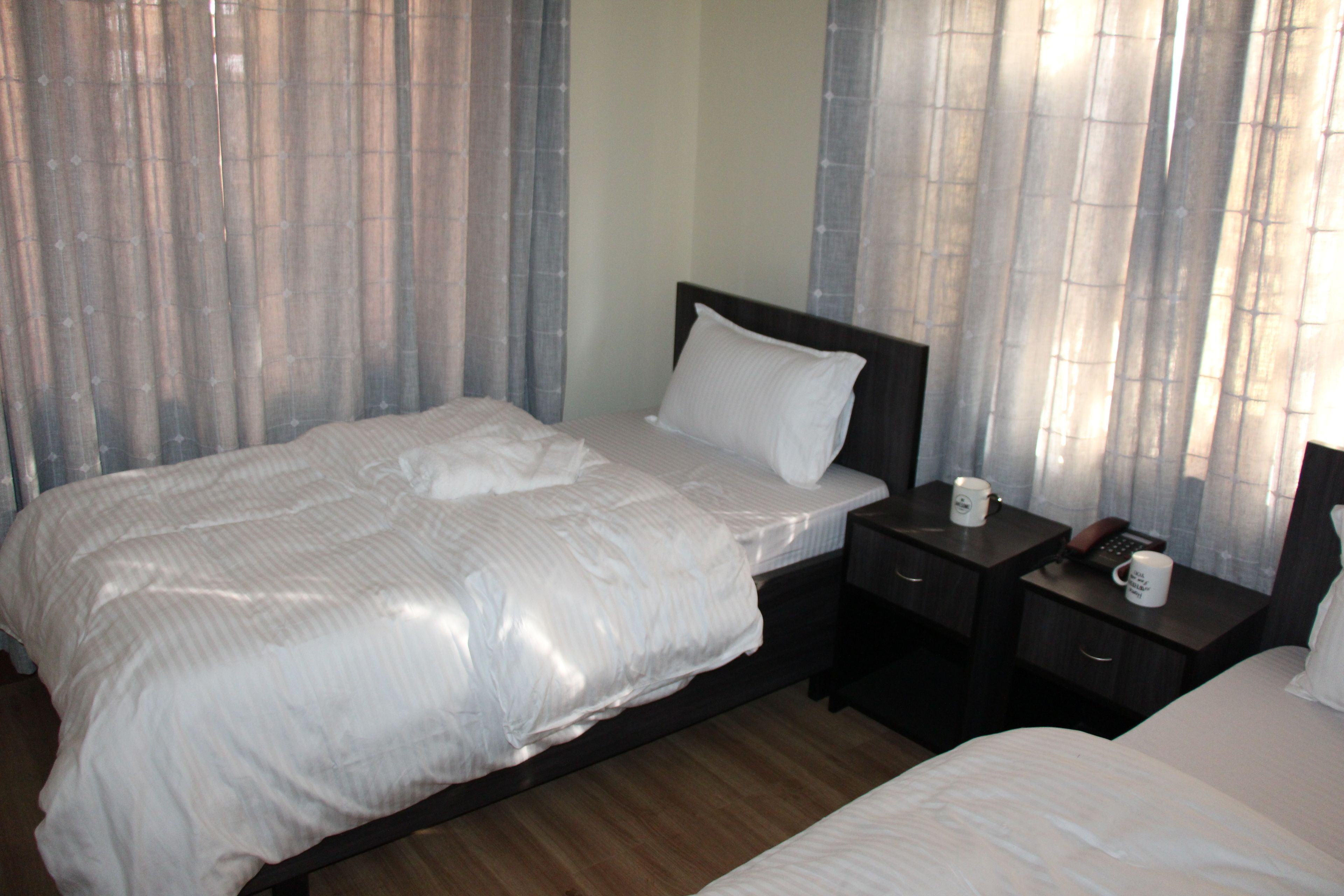 Habitación de hotel con una cama grande, una mesita de noche con lámpara y una ventana con cortinas.
