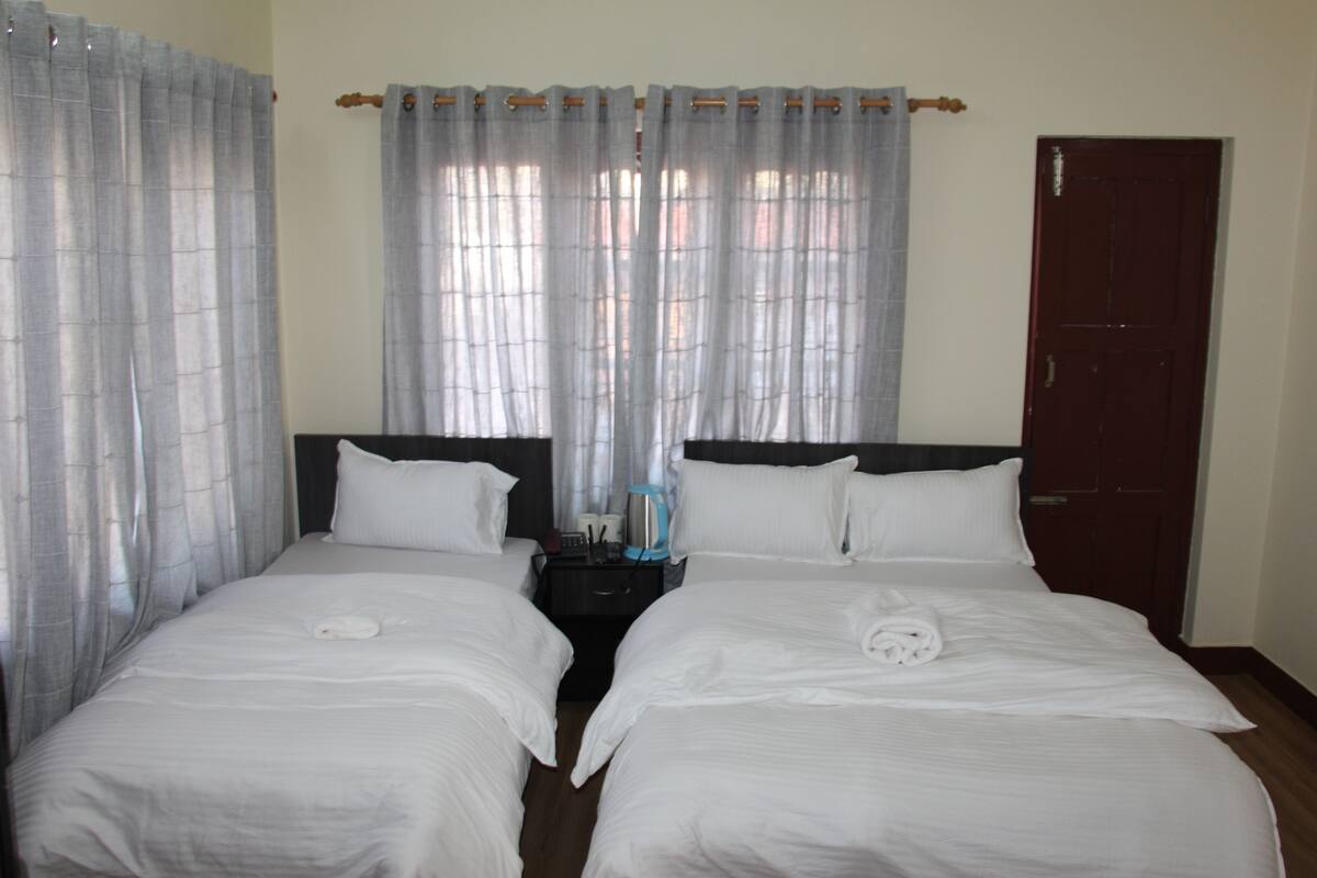 A hotel room with two beds, a nightstand, a coffee maker, and a door.