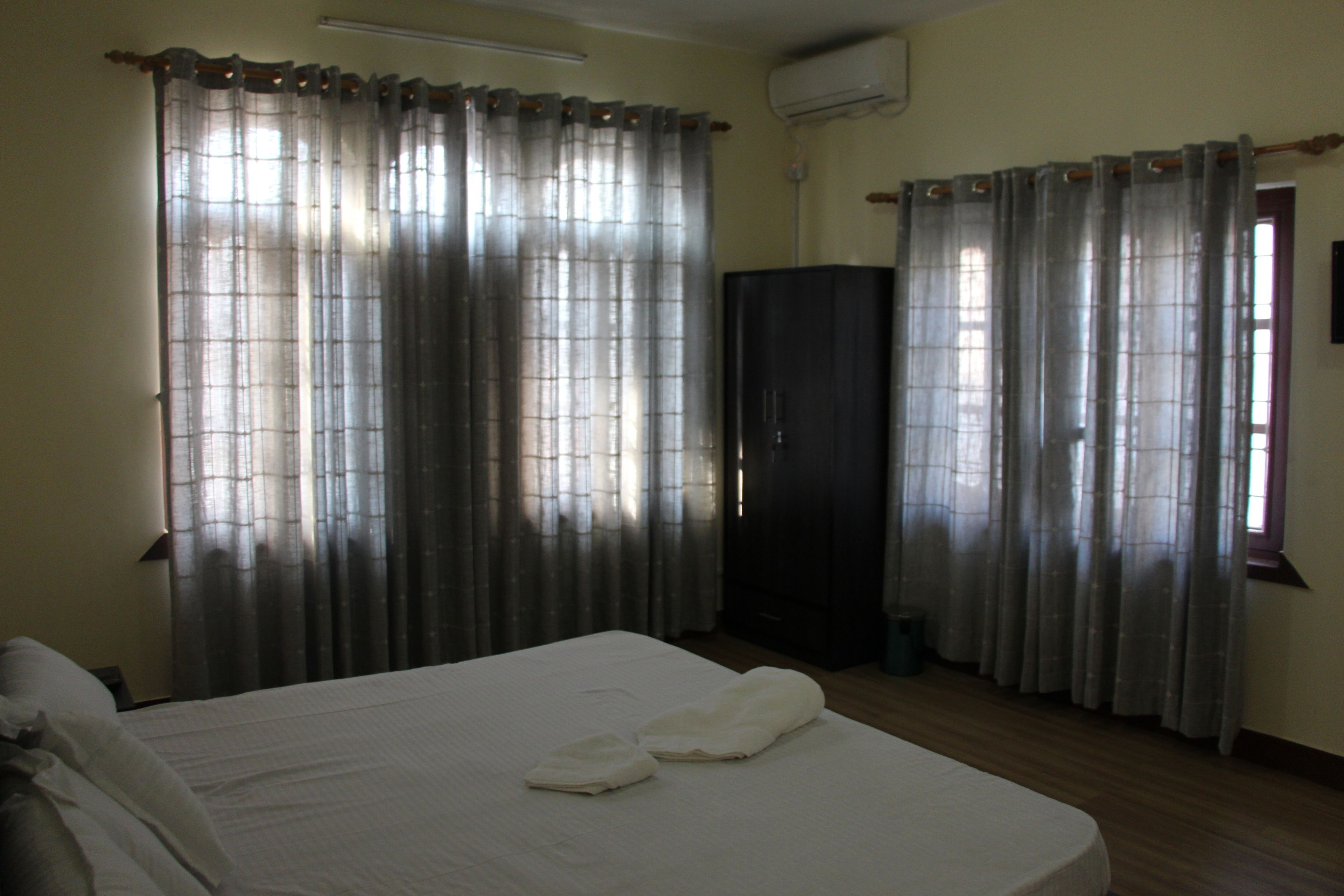 Quarto de hotel com cama, cortinas, um guarda-roupa e ar condicionado.