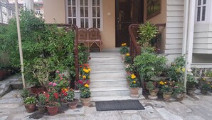 Una escalera de piedra que lleva a una puerta de madera con un panel de vidrio, rodeada de macetas con plantas y flores.