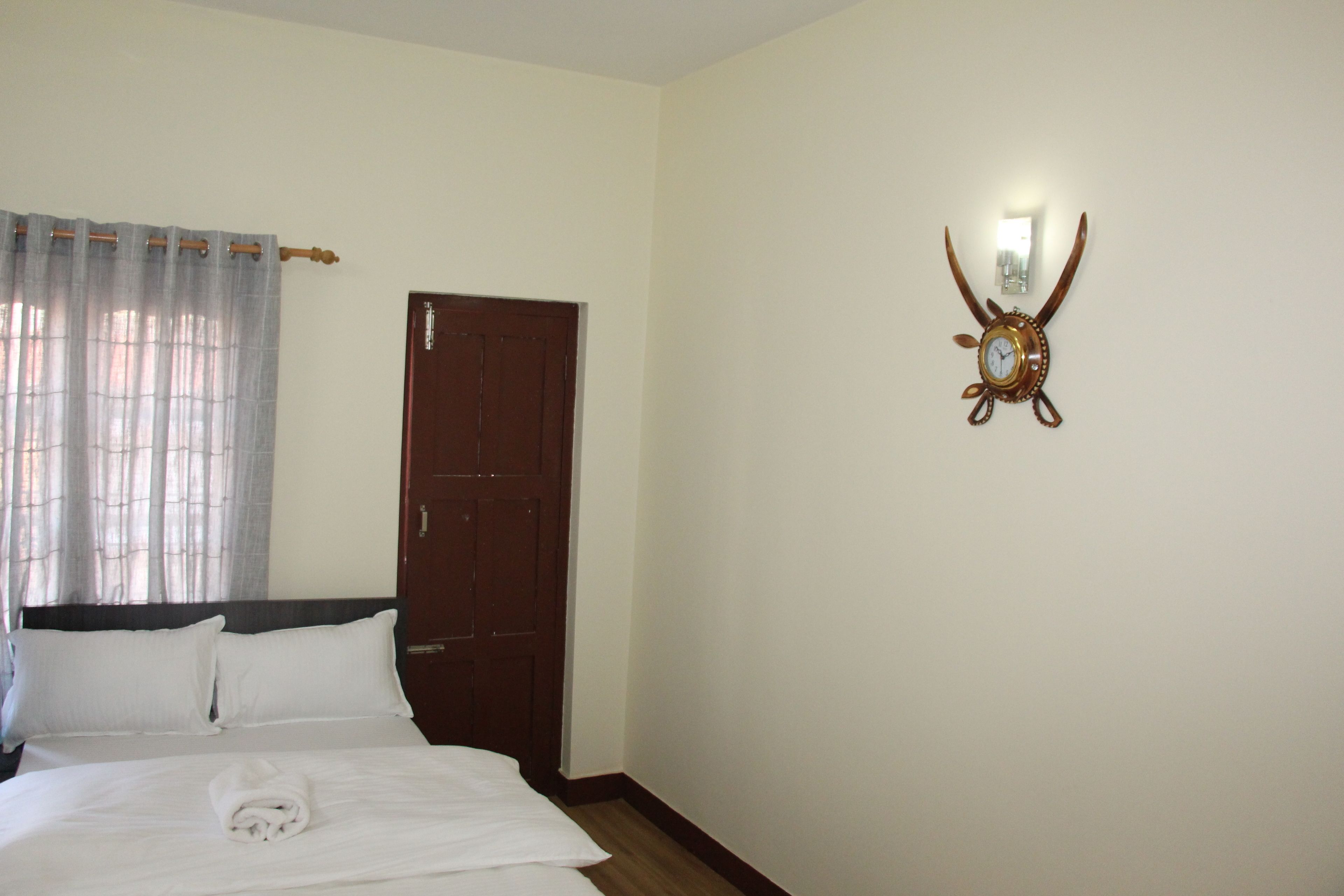 A hotel room with a bed, a wooden door, and a wall-mounted clock.