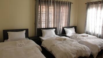 A hotel room with three single beds, each with white bedding and headboards.