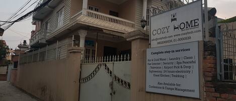 A two-story building with a sign advertising 'COZY HOME' services including laundry, internet, and 24-hour electricity.