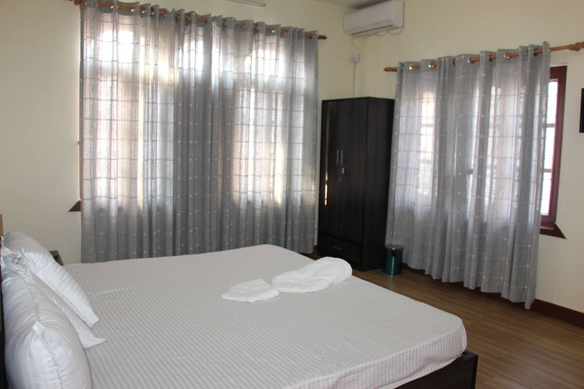 A hotel room with a large bed, two white pillows, a wooden floor, and a wardrobe.