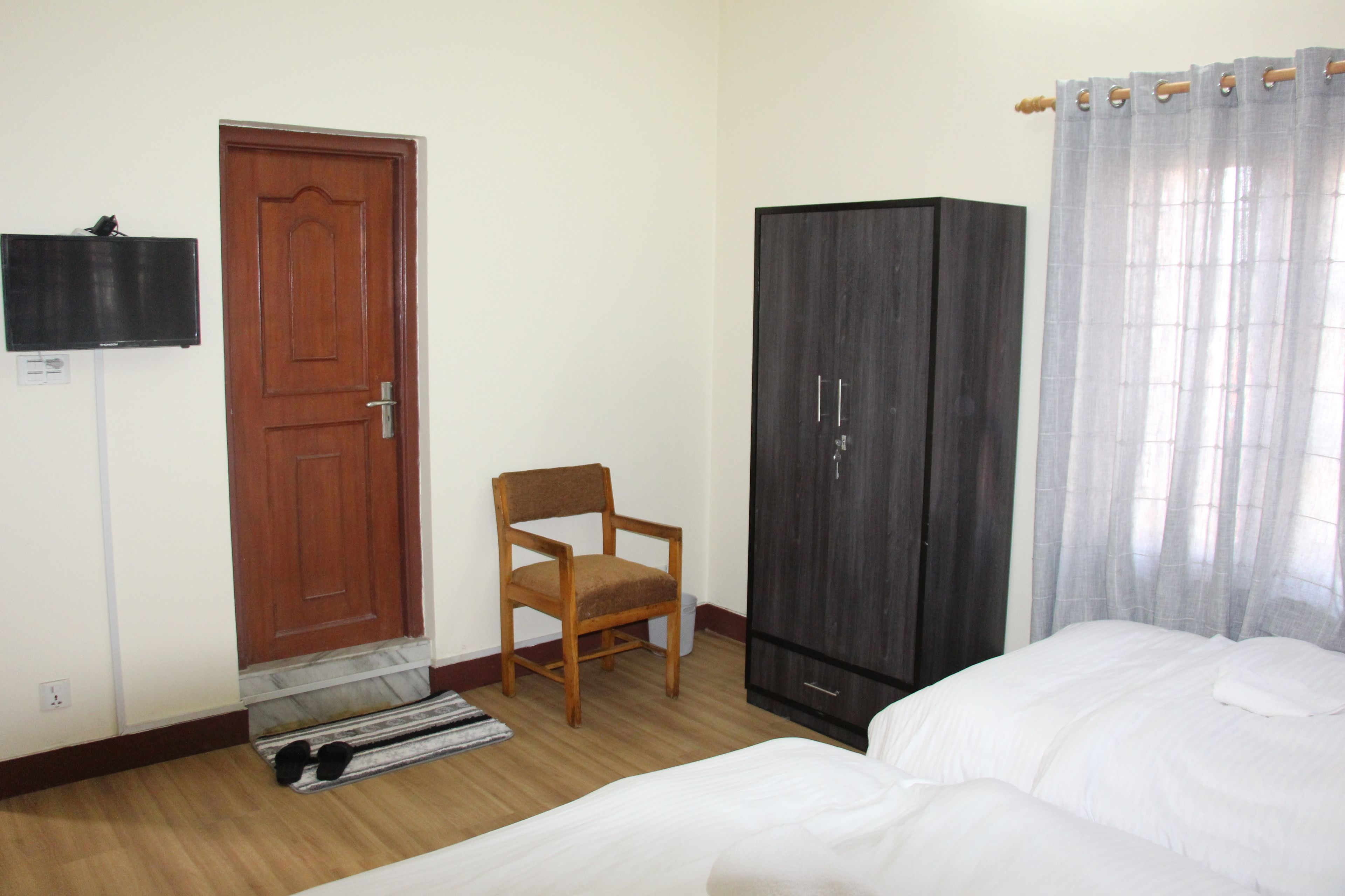 A bedroom with a bed, a wooden chair, a wardrobe, a door, and a television on the wall.