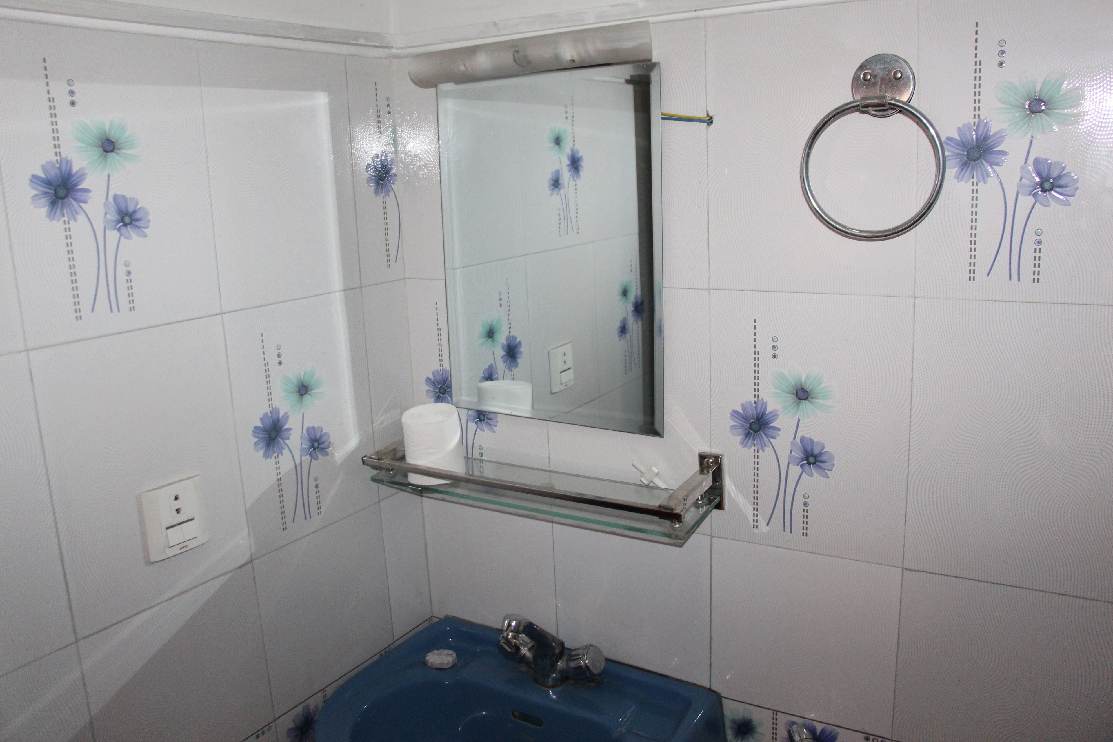 Un baño con lavamanos azul, estante de vidrio, espejo y azulejos con motivos florales.