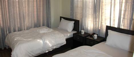 Habitación de hotel con dos camas, una mesita de noche con lámpara y una ventana con cortinas.