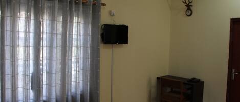 Una habitación con piso de madera, una mesa con una silla, una cortina, un reloj en la pared y una puerta.