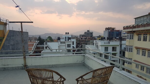 Una terraza en la azotea con dos sillones de mimbre y vistas a un paisaje urbano con edificios y montañas al fondo.