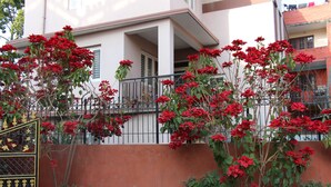 Un edificio con balcón, una reja negra y plantas de flores rojas.