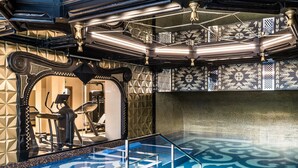 A modern indoor pool area with geometric tile patterns, exercise equipment, and a glass railing. - Hotel Wersal (Zakopane)