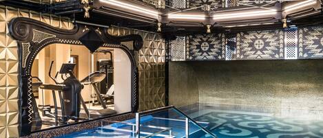 A modern indoor pool area with geometric tile patterns, exercise equipment, and a glass railing.