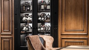 A room with a wooden cabinet containing wine bottles, a leather chair, and a patterned carpet. - Hotel Wersal (Zakopane)