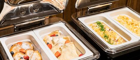 A buffet with various food items including pastries, fruits, and a casserole dish.
