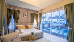 A spacious bedroom with a large bed, a sofa, and a view of an outdoor pool area. - Baan Marwin Hua Hin (Hua Hin)
