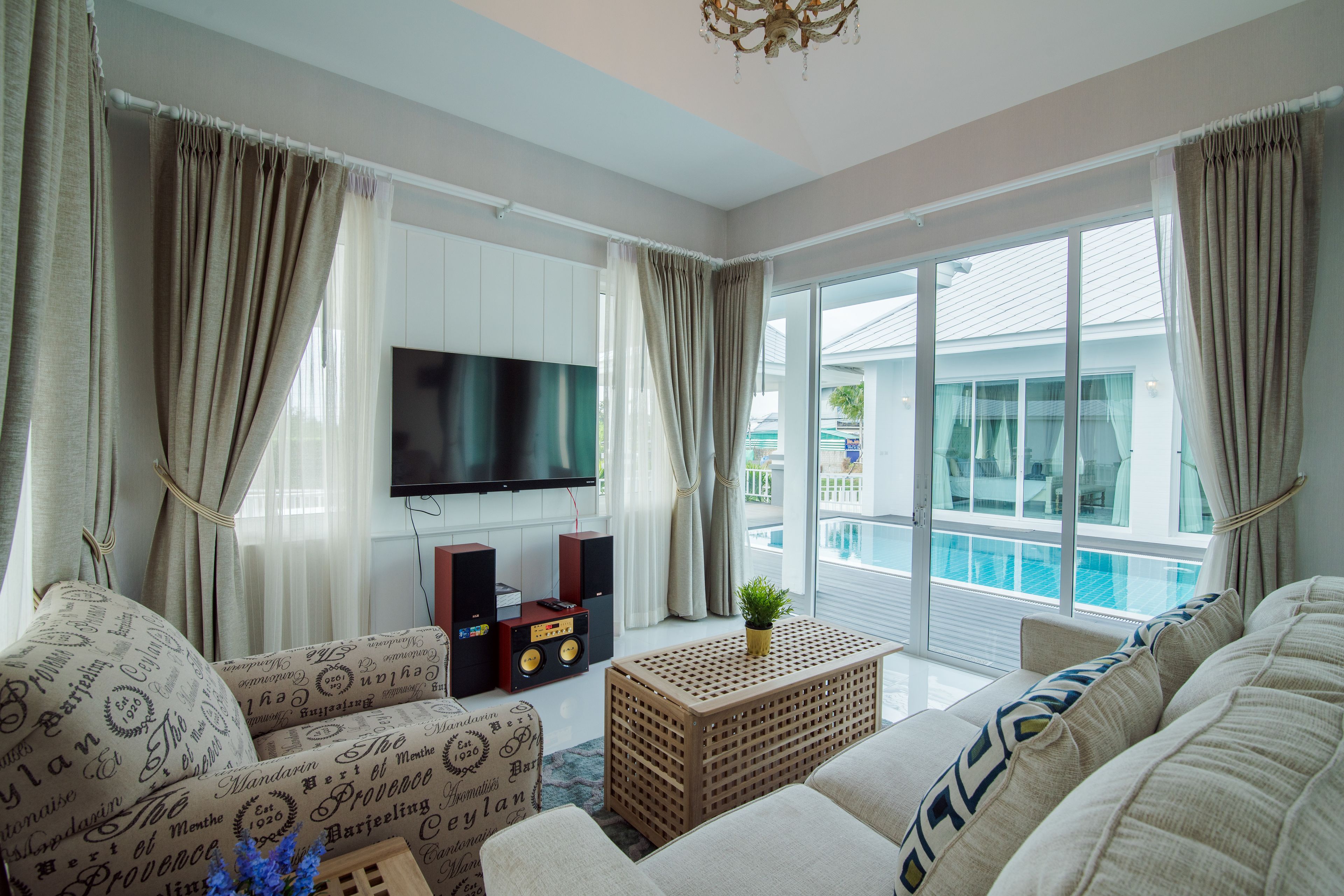 A modern living room with a flat-screen TV, speakers, and a large window overlooking a pool.