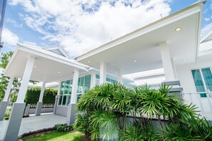 Un bâtiment moderne doté d’un porche, de grandes fenêtres et d’un jardin bien entretenu où poussent des plantes tropicales.