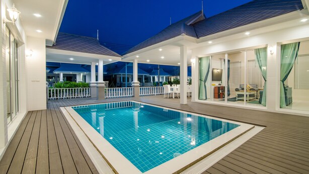 A swimming pool with a wooden deck, surrounded by a covered area with seating and a view of the sky. - Baan Marwin Hua Hin (Hua Hin)