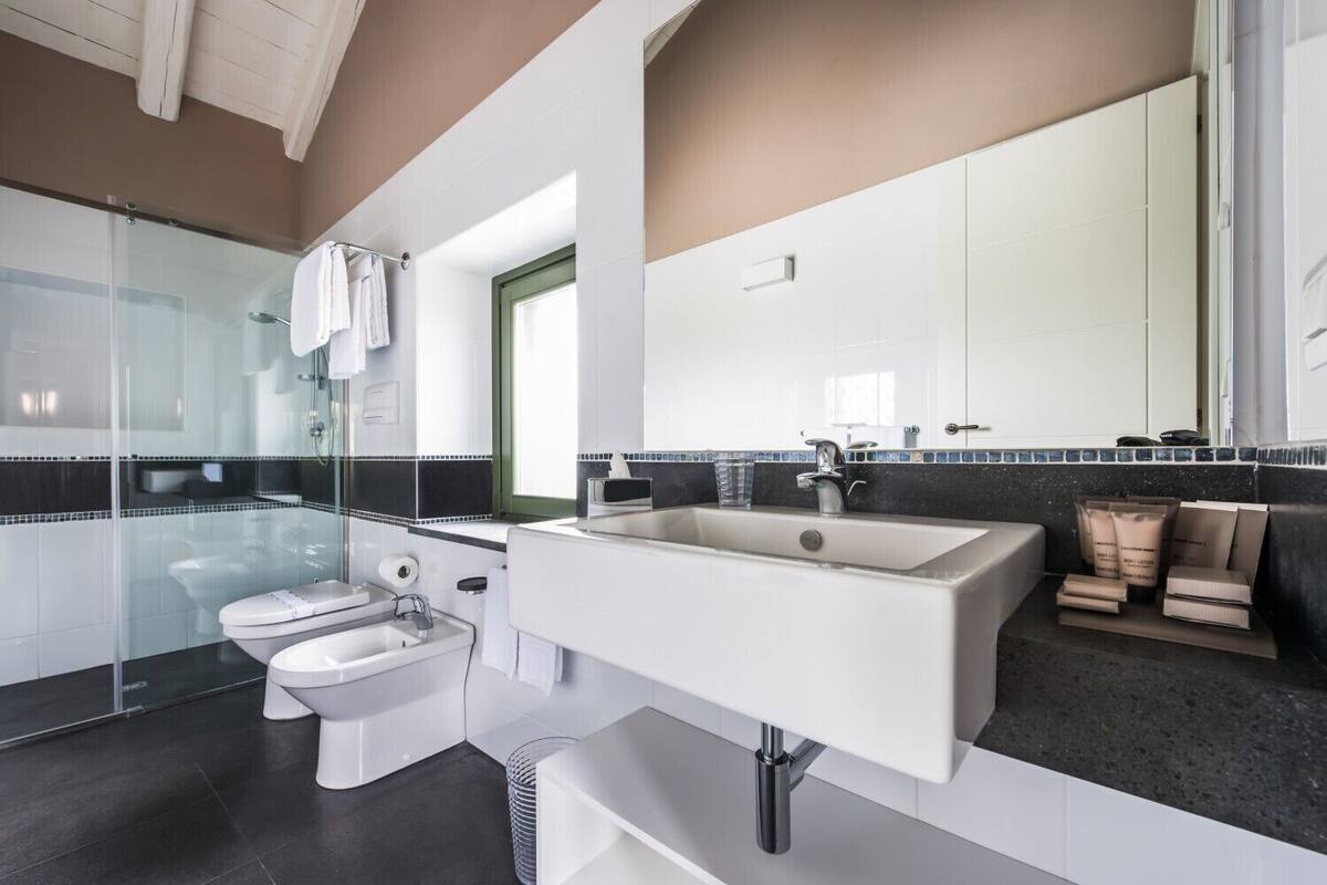 A modern bathroom with a glass shower enclosure, a white toilet, a large sink with a mirror, and a dark countertop.
