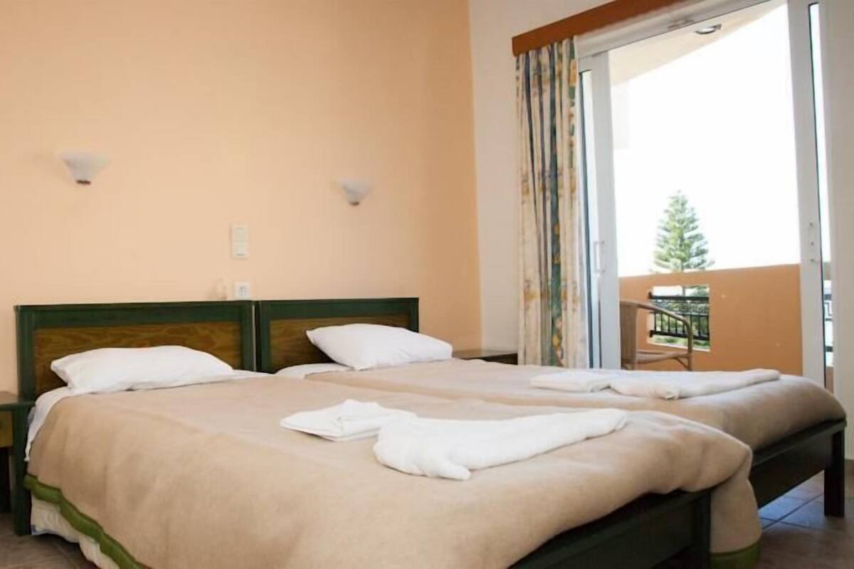 A double bed with two pillows, a nightstand, and a window with curtains.