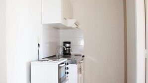A compact kitchen with white cabinets, a coffee maker, and a built-in oven. - Meandros (Apokoronas)