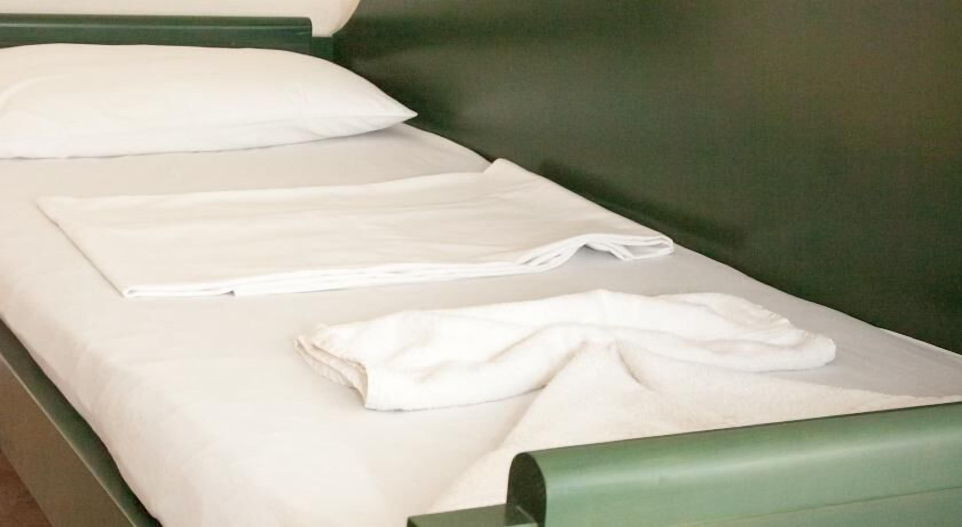 Un lit avec du linge de lit blanc et une serviette soigneusement pliée.