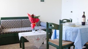 A dining area with a checkered sofa, a table with a floral tablecloth, and a bottle of wine. - Meandros (Apokoronas)
