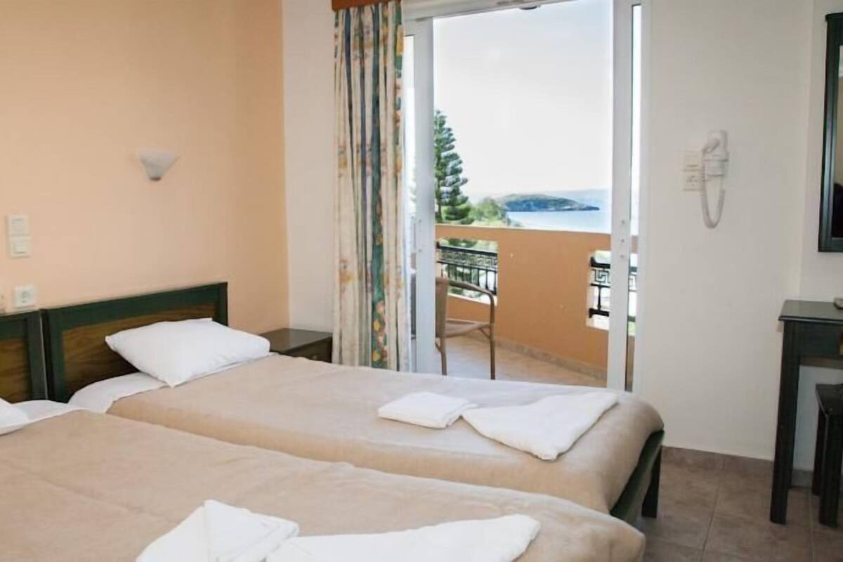 A hotel room with two beds, a balcony with a view, and a small table with a chair.