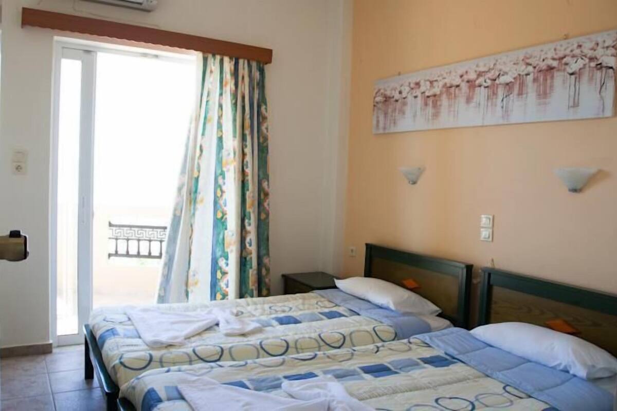 A hotel room with a bed, a balcony with a view, and a painting on the wall.