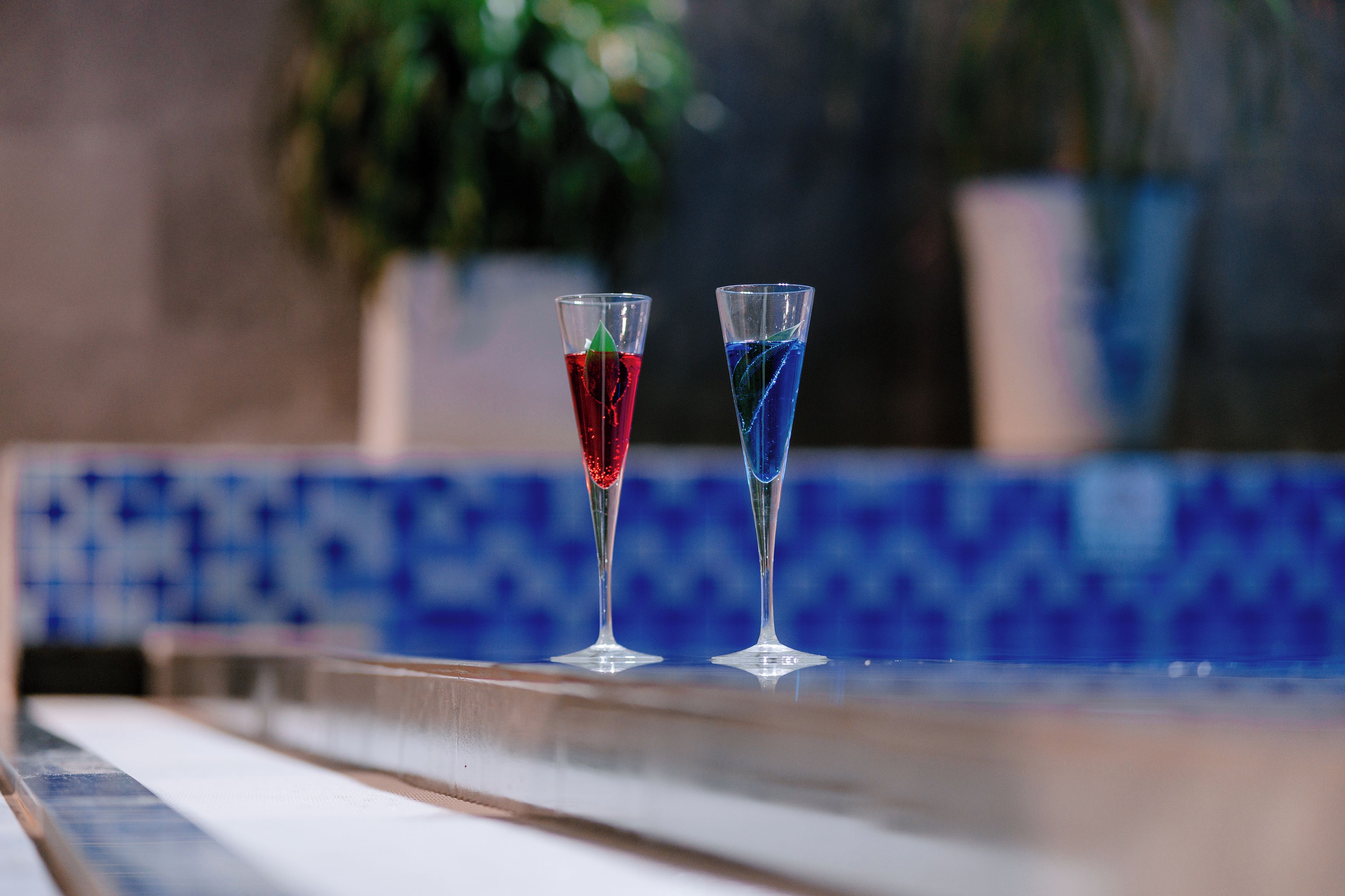 Two glasses of red and blue beverages on a tiled surface.