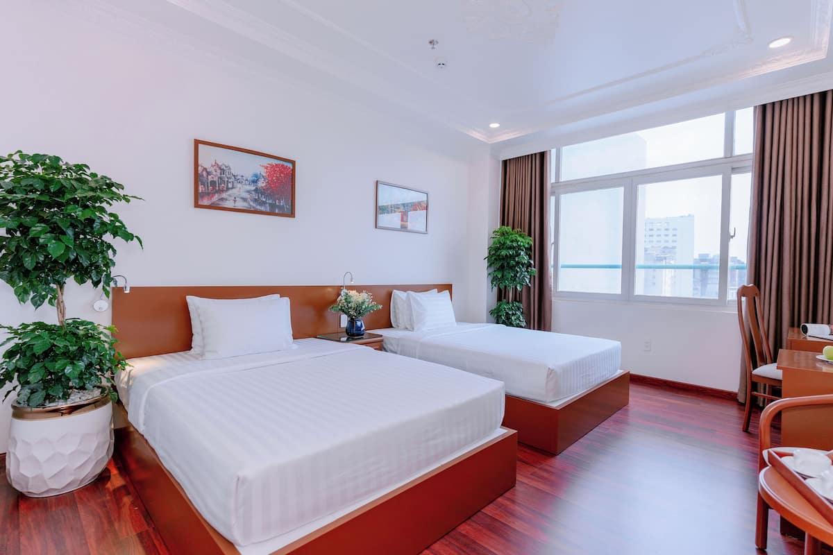 Une chambre d’hôtel avec deux lits, une grande fenêtre avec des rideaux et deux plantes en pot.