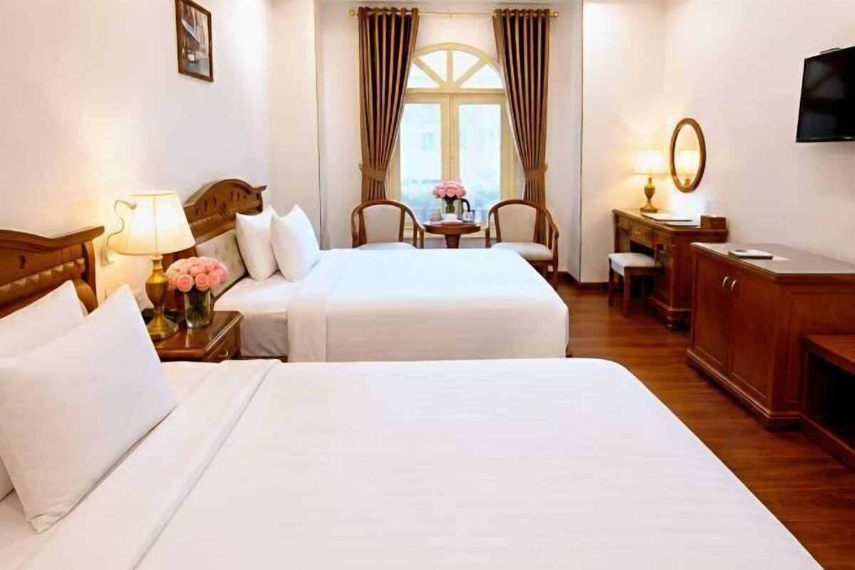 Une chambre d’hôtel avec deux lits, un bureau, une chaise, une télévision et une fenêtre avec des rideaux.