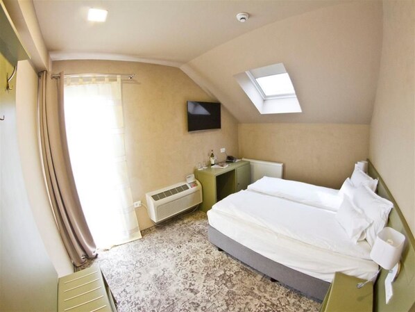 A hotel room with a bed, a desk, a chair, a radiator, a television, and a skylight. - Pensiunea Sarea-n Bucate (Turda)