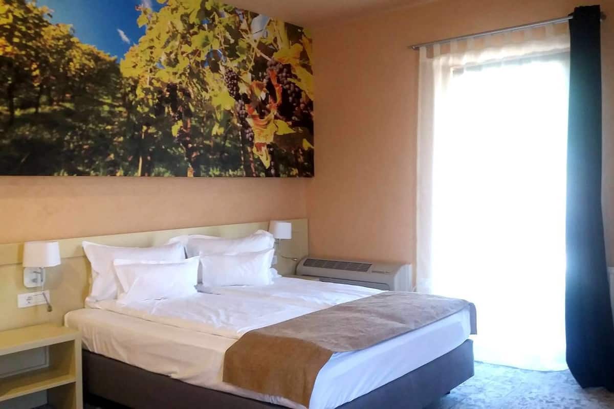 Une chambre d’hôtel avec un grand lit, des tables de chevet, un climatiseur fixé au mur et une fenêtre avec des rideaux.