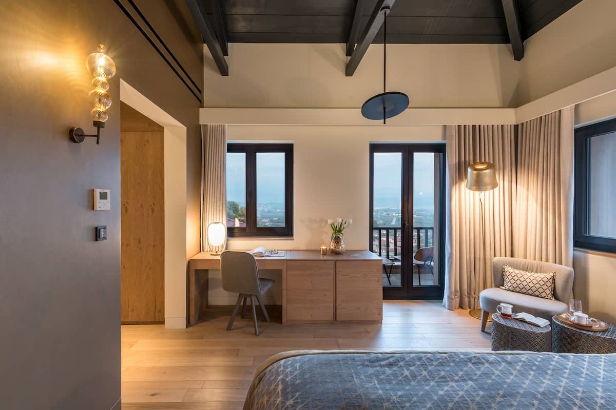 Une chambre d’hôtel moderne, dotée d’un bureau en bois, d’un fauteuil confortable, d’un lit et d’un balcon avec vue.