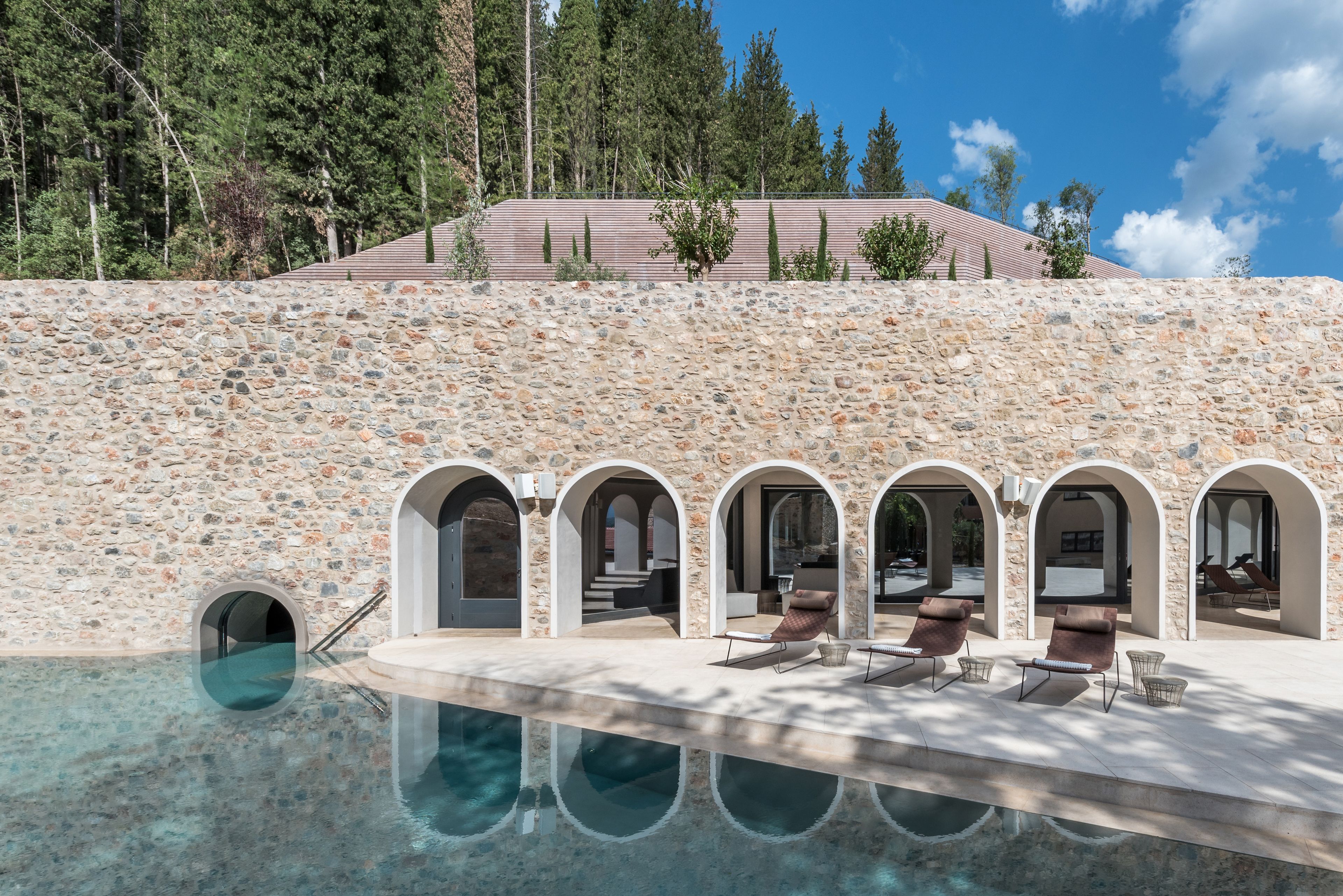 A stone wall with a pool and lounge chairs.