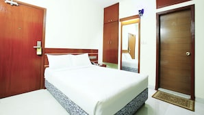 A hotel room with a bed, wooden wardrobe, a mirror, and a door.