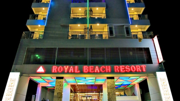 A multi-story building with balconies, a sign reading "ROYAL BEACH RESORT", and a car parked in front.
