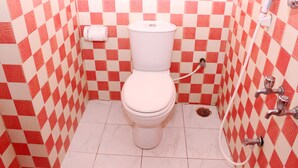 Une salle de bain avec un carrelage à motifs à carreaux rouges et blancs, des toilettes blanches et une douche avec un flexible.