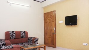 Un salon avec un canapé, une table basse, une porte en bois et un téléviseur fixé au mur.